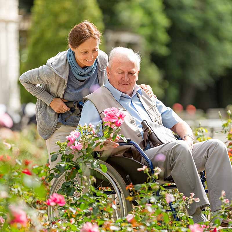 Caregiver and senior man on a wheelchair walking outdoors